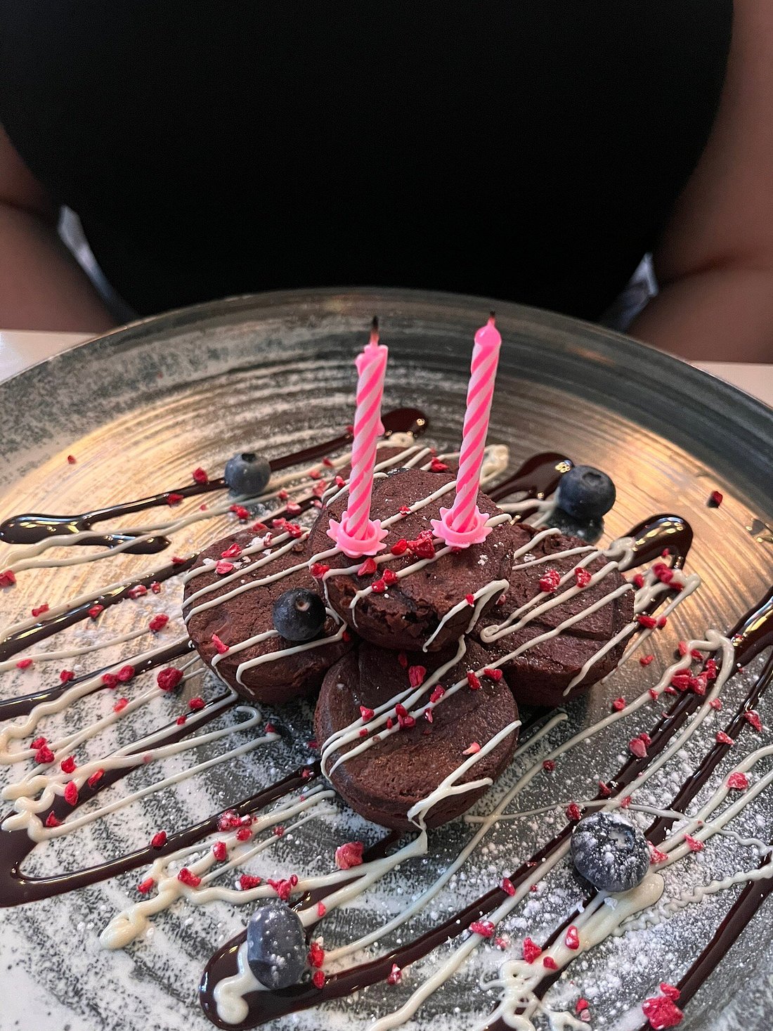 Chocolate brownies topped with white chocolate drizzle, berries, and pink birthday candles.


