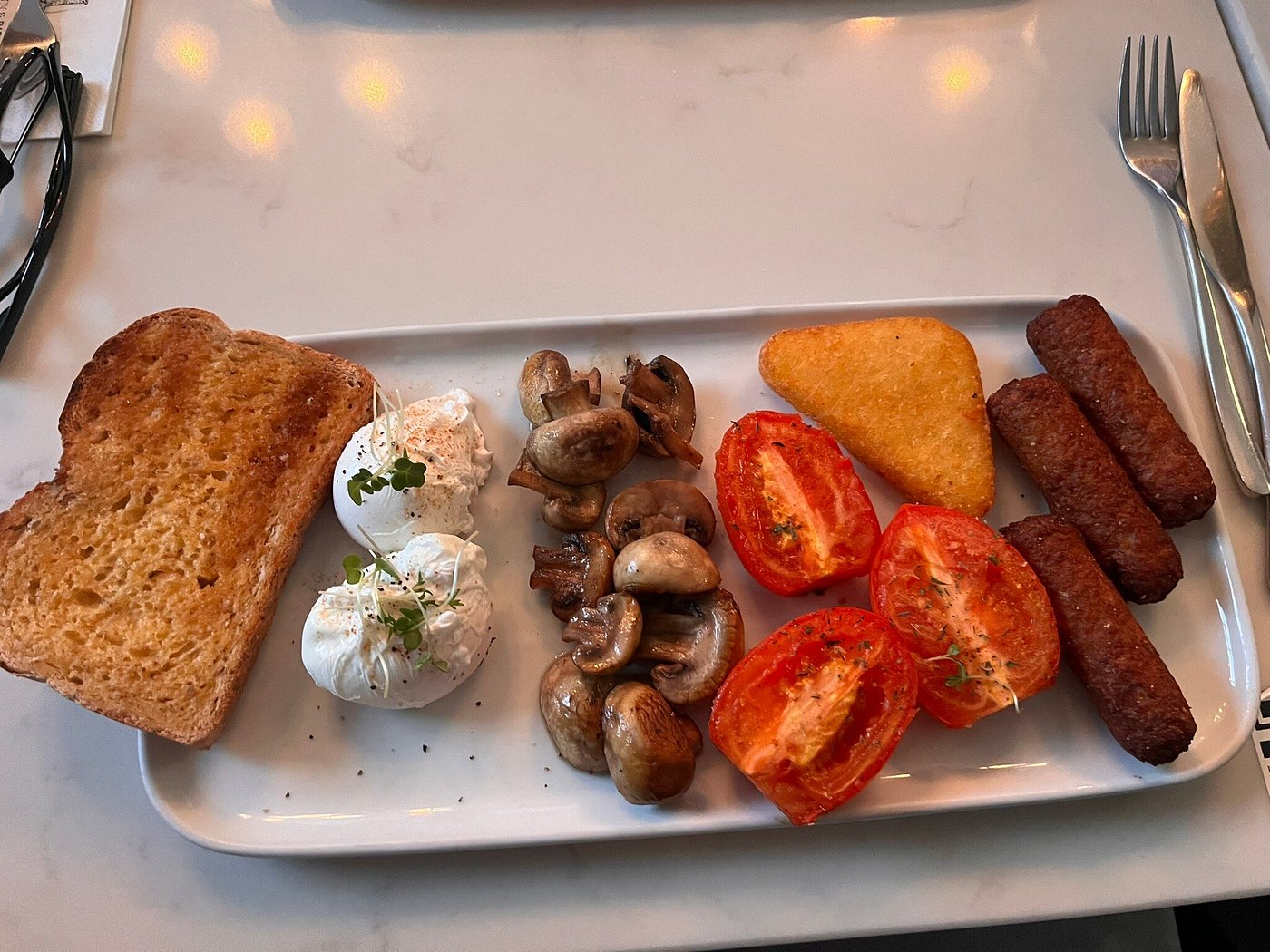  Vegetarian breakfast with veggie sausages, poached eggs, mushrooms, grilled tomato, hash brown, and toast.