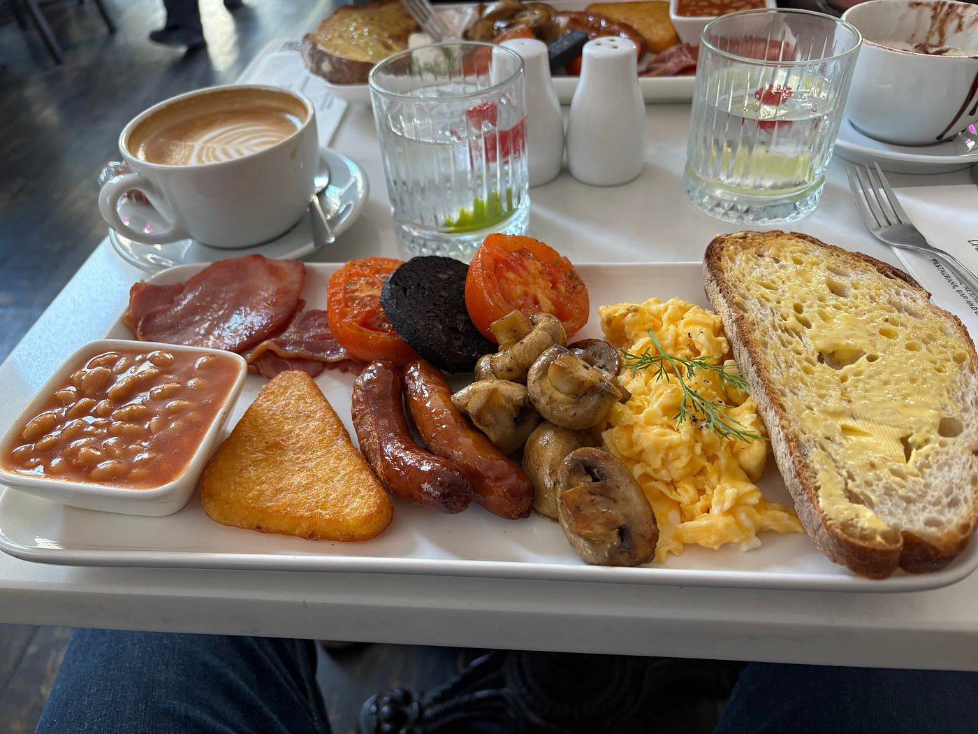 Full English breakfast with scrambled eggs, buttered toast, hash brown, sausage, bacon, black pudding, tomato, mushrooms, and baked beans.