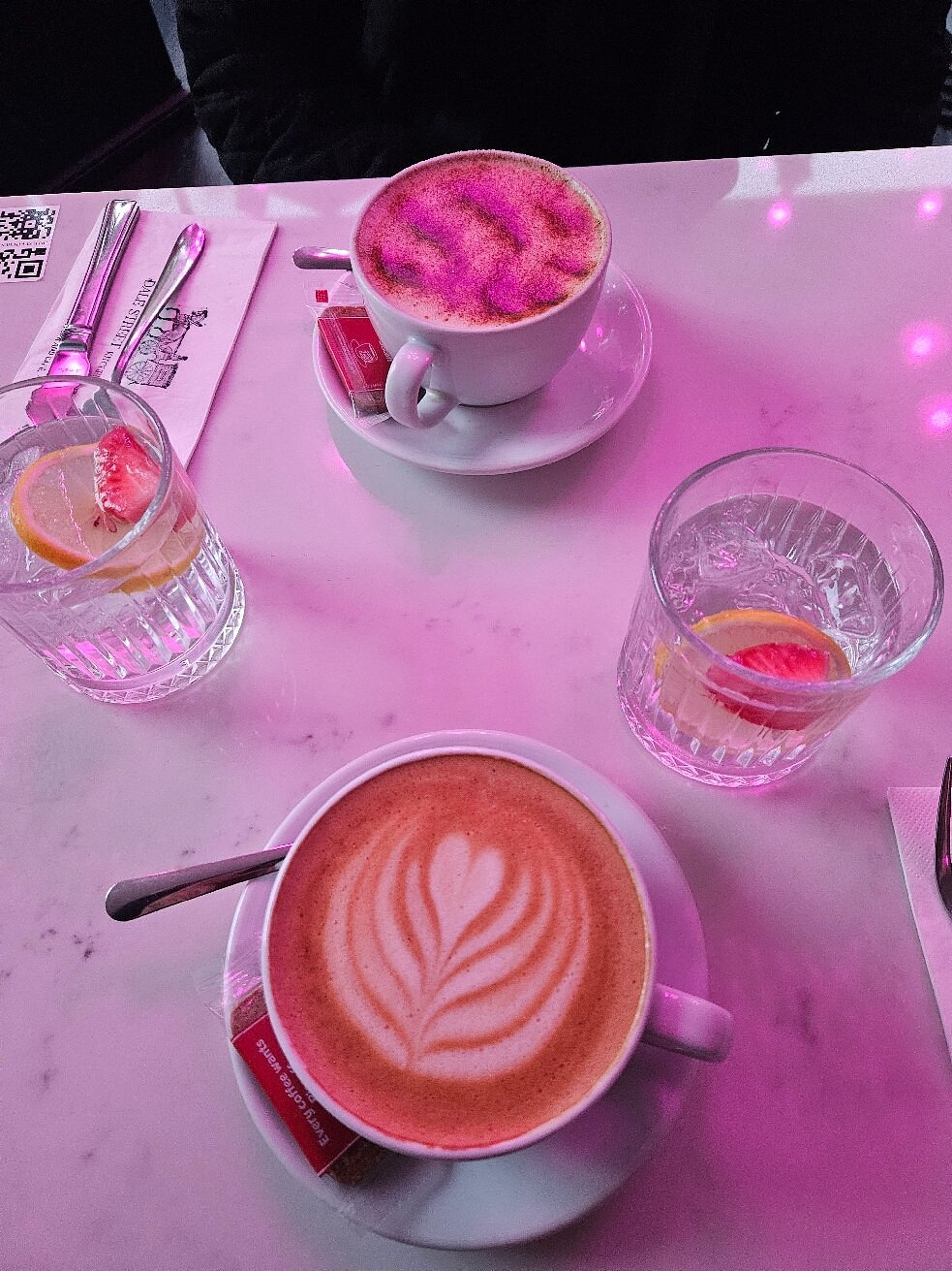Cappuccino with heart-shaped latte art beside glasses of lemon water on a white marble table.