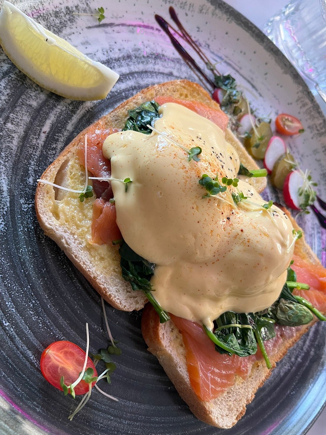 Eggs Benedict with poached egg, hollandaise, spinach, and smoked salmon on toast, garnished with salad and lemon.