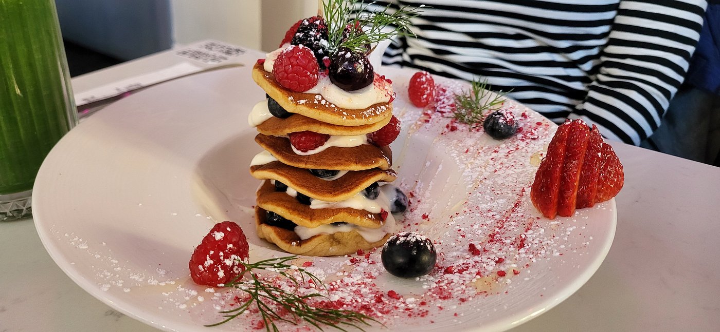 Mini pancake stack layered with yogurt, raspberries, blueberries, and powdered sugar, garnished with dill and strawberries.