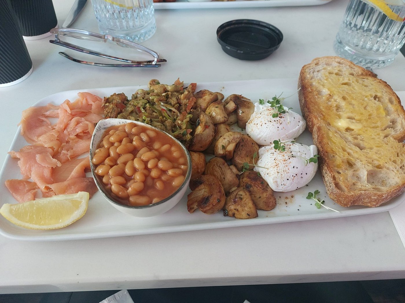 Breakfast plate with smoked salmon, baked beans, sautéed mushrooms, poached eggs, toast, and aubergine mash.